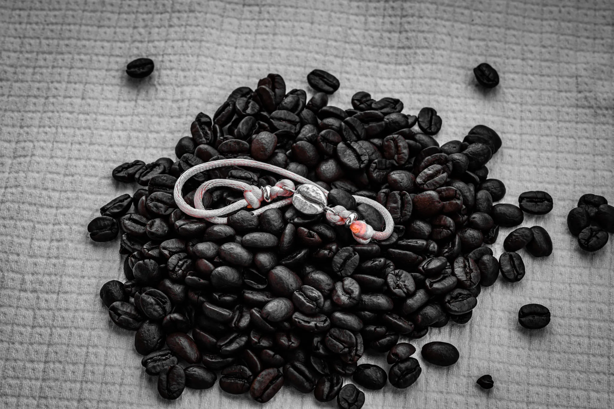 Le bracelet « Le grain » posé sur un tas de grains de café torréfiés.